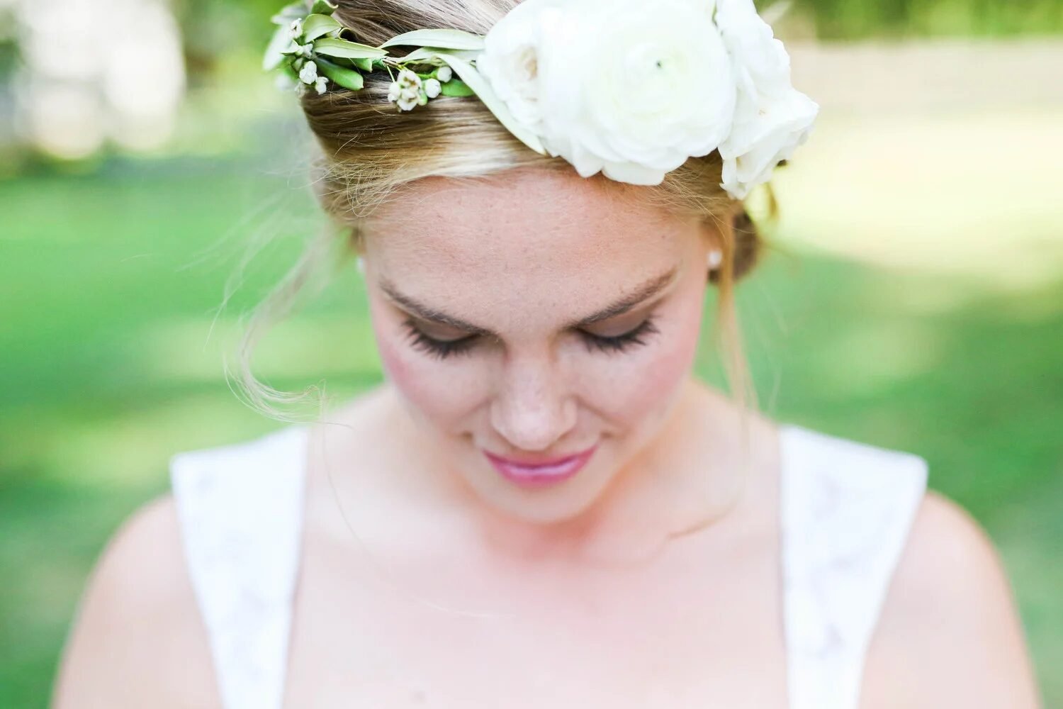 Dreamy close portrait of a bride looking down, white ranunculus and greenery floral crown