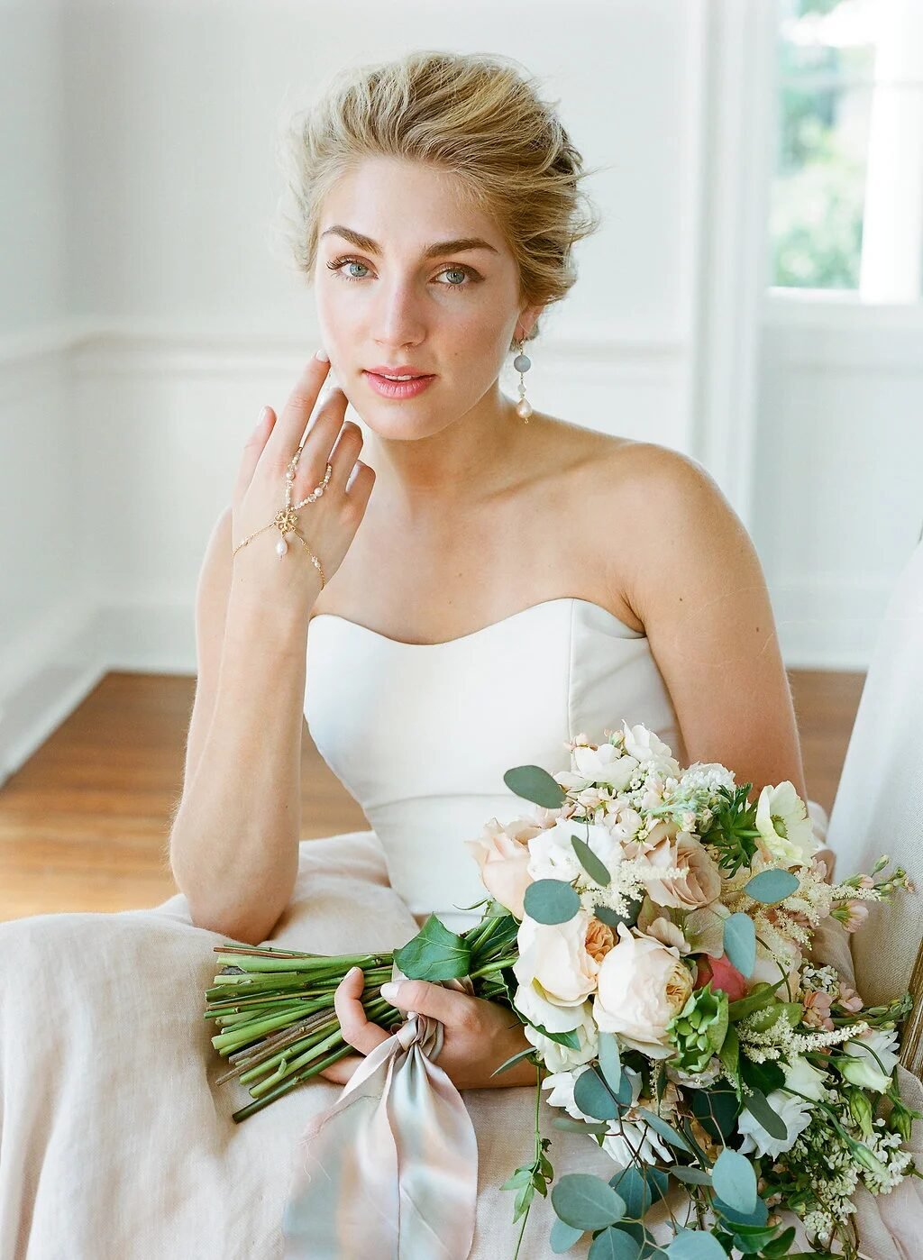 Intimate seated bride portrait holding soft ivory-and-eucalyptus bouquet, hand to cheek, film tones