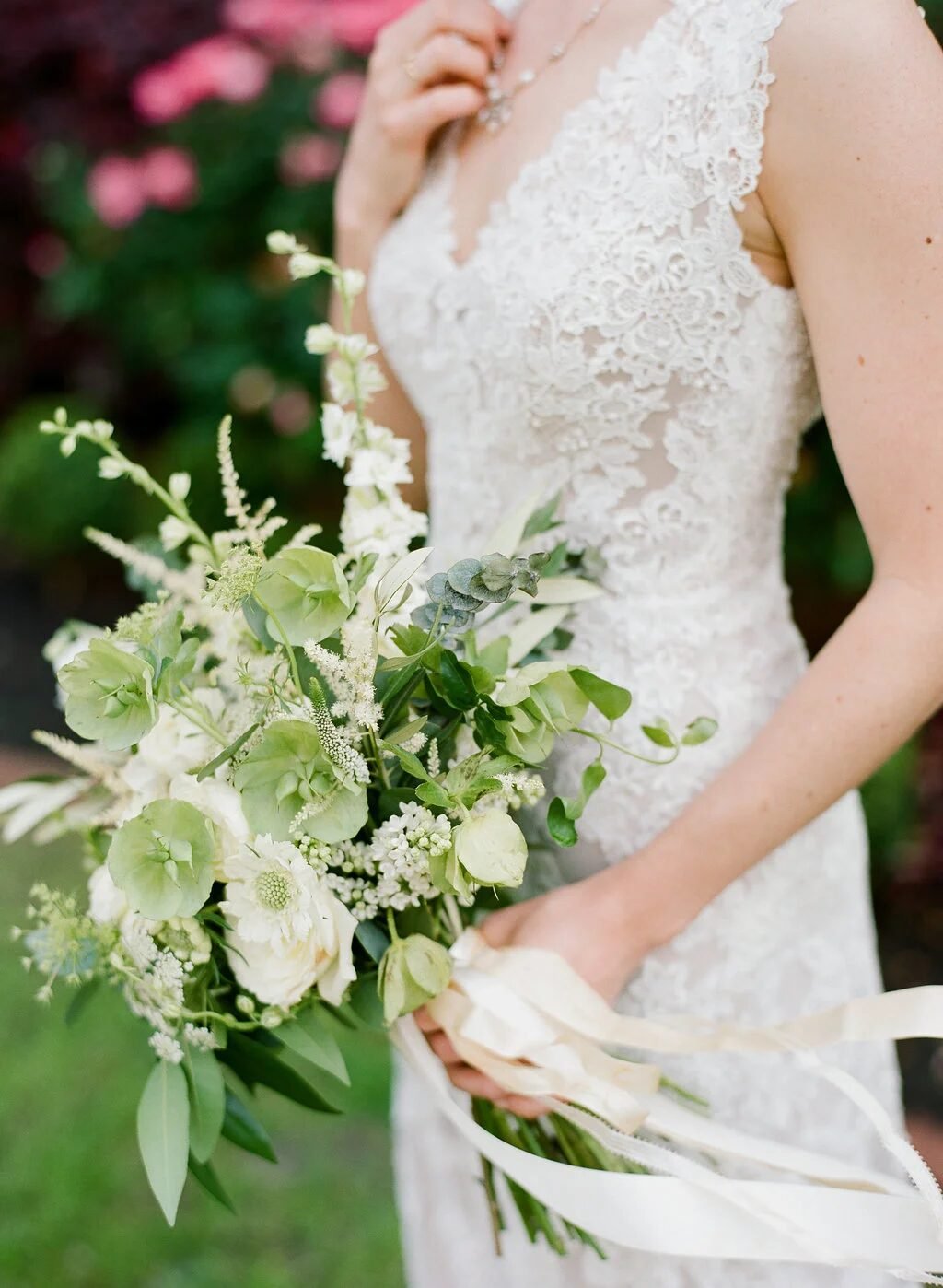 Side view of bride holding an organic green-and-white bouquet with ivory ribbon streamers, lace gown